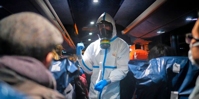 Een militaire officier in een beschermend pak geeft instructies aan evacués uit Wuhan, China, terwijl ze naar het ziekenhuis reizen na aankomst op een militaire basis in Wroclaw, Polen.  (AP Foto/Arek Rataj, Bestand)