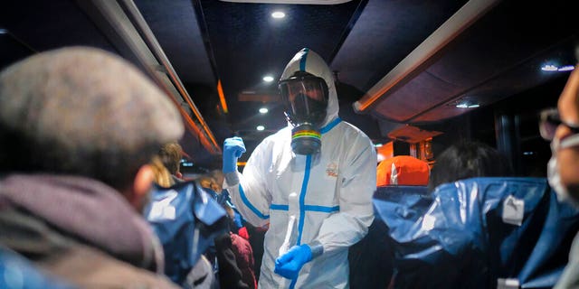 A military officer wearing a protective suit gives instructions to evacuees from Wuhan, China, as they travel to a hospital after their arrival at a military base in Wroclaw, Poland. (AP Photo/Arek Rataj, File)