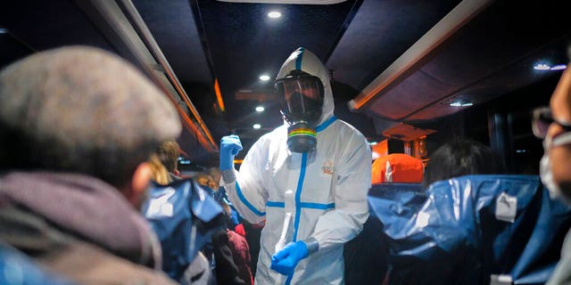 FILE - In this Feb. 2, 2020 file photo, a military officer wearing a protective suit gives instructions to evacuees from Wuhan, China, as they travel to a hospital after their arrival at a military base in Wroclaw, Poland. (AP Photo/Arek Rataj, File)