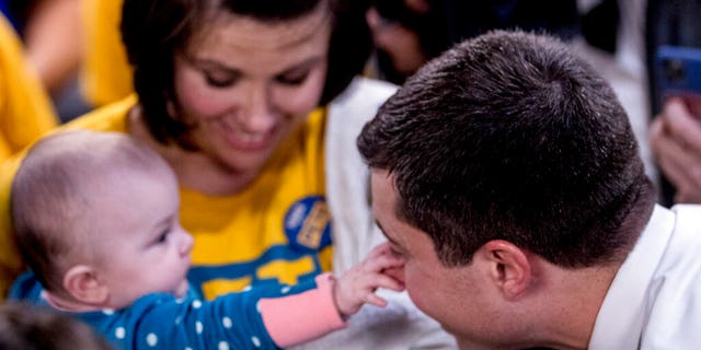 Tara Hansen of West Des Moines, Iowa, holds her granddaughter Emmy who grabs the nose of Democratic presidential candidate former South Bend, Ind., Mayor Pete Buttigieg as he visits supporters at a campaign office the day of the Iowa Caucus, Monday, Feb. 3, 2020, in West Des Moines, Iowa. (AP Photo/Andrew Harnik)