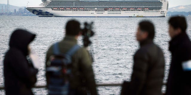 A TV crew film a cruise ship Diamond Princess anchoring off the Yokohama Port Tuesday, Feb. 4, 2020. (AP Photo/Eugene Hoshiko)