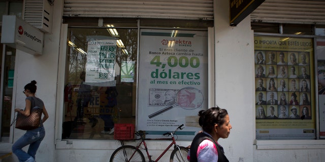 FILE - In this April 5, 2016 file photo, pedestrians walk past signs advertising money transfer services and loans, outside a business in Mexico City. Mexican migrants working abroad sent home a record $36 billion in remittances in 2019, the country's central bank reported Tuesday, Feb. 4, 2020. (AP Photo/Rebecca Blackwell, File)