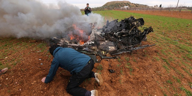 Rebel fighters look at a Syrian government helicopter that was shot down in Idlib province, Syria, Tuesday, Feb. 11, 2020. (AP Photo/Ghaith Alsayed)