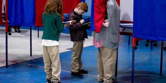 Samantha Murch accompanied by her two boys Alexander, 8, center, and Jacob, 11, left, votes in the New Hampshire primary at Bishop O'Neill Youth Center, Tuesday, Feb. 11, 2020, in Manchester, N.H. (AP Photo/Andrew Harnik)