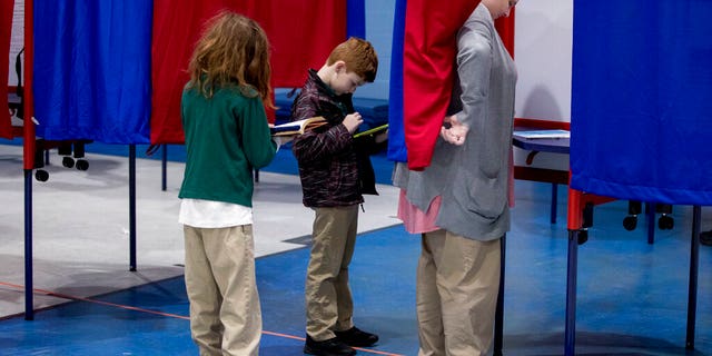 Samantha Murch accompanied by her two boys Alexander, 8, center, and Jacob, 11, left, votes in the New Hampshire primary at Bishop O'Neill Youth Center, Tuesday, Feb. 11, 2020, in Manchester, N.H. (AP Photo/Andrew Harnik)