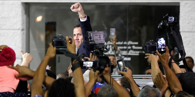 Surrounded by the media, opposition leader Juan Guaido pumps his fist after a rally at Bolivar Plaza in Chacao, Venezuela, Tuesday, Feb. 11, 2020. Guaido returned home from a tour of nations that back his effort to oust socialist leader Nicolas Maduro. (AP Photo/Ariana Cubillos)