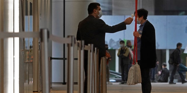 A security guard wearing a protective face mask checks the temperature of a cleaning woman in Hong Kong, Friday, Feb. 14, 2020. COVID-19 viral illness has sickened tens of thousands of people in China since December. (AP Photo/Vincent Yu)