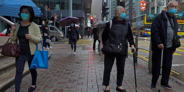 People wearing protective face masks walk on a street in the rain in Hong Kong, Friday, Feb. 14, 2020. COVID-19 viral illness has sickened tens of thousands of people in China since December. (AP Photo/Vincent Yu)