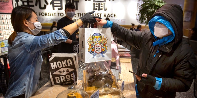 Manager Chen Tiantian, left, hands a takeaway order to a delivery driver at a Moka Bros cafe in Beijing, Friday, Feb. 14, 2020. (AP Photo/Mark Schiefelbein)