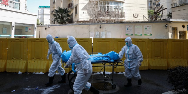 Medical workers move a person who died from COVID-19 at a hospital in Wuhan in central China's Hubei province on Sunday. Chinese authorities on Monday reported a slight upturn in new virus cases and hundred more deaths for a total of thousands since the outbreak began two months ago. (Chinatopix via AP)