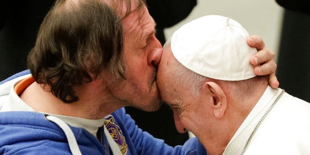 Pope Francis is kissed by a man during his weekly general audience, at the Pope Paul VI hall, at the Vatican, Wednesday, Feb. 19, 2020.