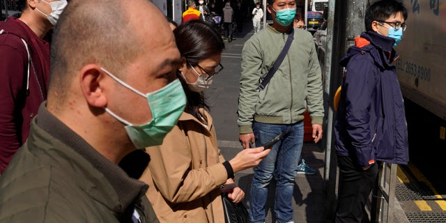 People wearing face masks walk on a down own street in Hong Kong Friday, Feb. 21, 2020. COVID-19 viral illness has sickened tens of thousands of people in China since December. (Associated Press)