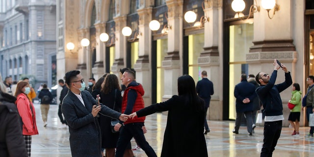 Tourists wearing sanitary masks move a few steps of dance, in downtown Milan, Italy, Sunday, Feb. 23, 2020. (AP Photo/Antonio Calanni)