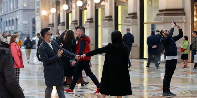 Tourists wearing sanitary masks move a few steps of dance, in downtown Milan, Italy, Sunday, Feb. 23, 2020. (AP Photo/Antonio Calanni)