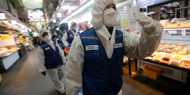 Workers wearing protective gears arrive to spray disinfectant as a precaution against the coronavirus at a market in Seoul, South Korea, Monday, Feb. 24, 2020. South Korean President Moon Jae-in said his government had increased its anti-virus alert level by one notch to “Red,” the highest level. It allows for the temporary closure of schools and reduced operation of public transportation and flights to and from South Korea. (AP Photo/Ahn Young-joon)