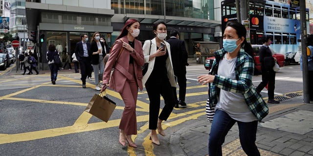 People wearing masks, walk across a street in Hong Kong, Monday, Feb. 24, 2020. The COVID-19 viral illness has sickened thousands of people throughout China and other countries since December. (AP Photo/Kin Cheung)