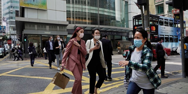 People wearing masks, walk across a street in Hong Kong, Monday, Feb. 24, 2020. The COVID-19 viral illness has sickened thousands of people throughout China and other countries since December. (AP Photo/Kin Cheung)
