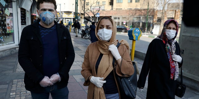 Tehran resident Leila Tayyeb, center, with her husband wearing mask and gloves, speaks with The Associated Press, as a woman walks past, in downtown Tehran, Iran, Thursday, Feb. 27, 2020. (AP Photo/Vahid Salemi)