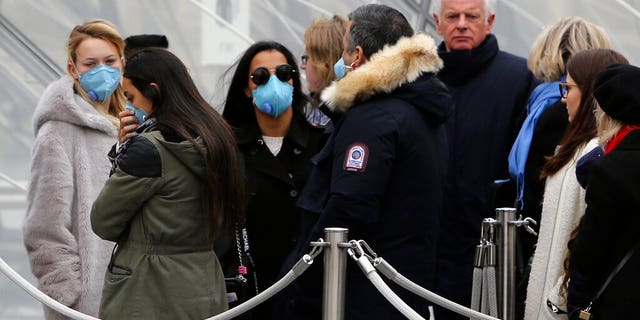 Tourists, some wearing a mask, queue to enter the Louvre museum Friday, Feb. 28, 2020 in Paris.