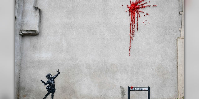 A woman walks past a new artwork on the side of a house in Bristol, England, Thursday Feb. 13, 2020, which has been confirmed as the work of street artist Banksy. (Ben Birchall/PA via AP)