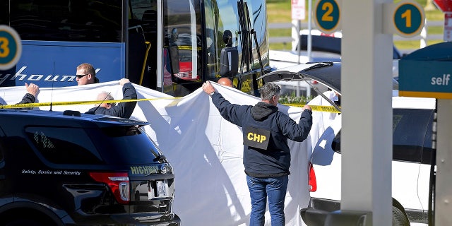 Coroner's officials work behind a drape to remove the body of a person who was killed when a gunman opened fire aboard a packed Greyhound bus, and wounded five others before the driver pulled over onto the shoulder and the killer got off, in Lebec, Calif., Monday. (AP Photo/Jayne Kamin-Oncea)