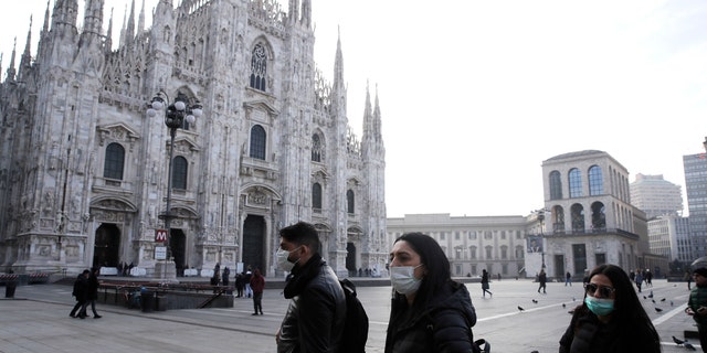 People wearing sanitary masks walk past the Duomo gothic cathedral in Milan, Italy, Sunday, Feb. 23, 2020.