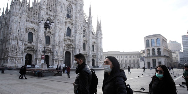 People wearing sanitary masks walk past the Duomo gothic cathedral in Milan, Italy, Sunday, Feb. 23, 2020.