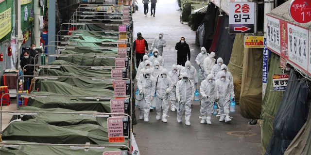 Workers wearing protective gear spray disinfectant as a precaution against the COVID-19 coronavirus in a local market in Daegu, South Korea, Sunday, Feb. 23, 2020.