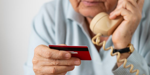 Femme utilisant un téléphone tout en tenant une carte de crédit.