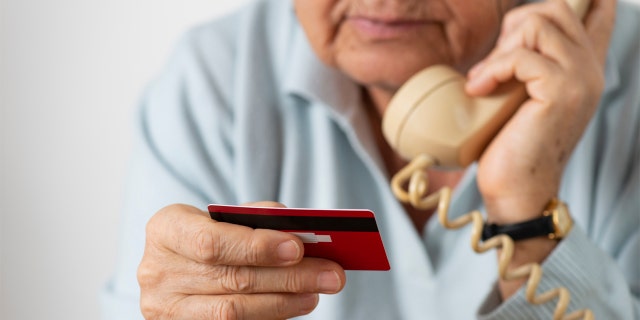 Femme utilisant un téléphone tout en tenant une carte de crédit.