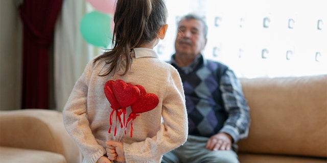 Cute little girl celebrating Valentine's day with parents, family and herself, holding heart shape decorations, home interior.