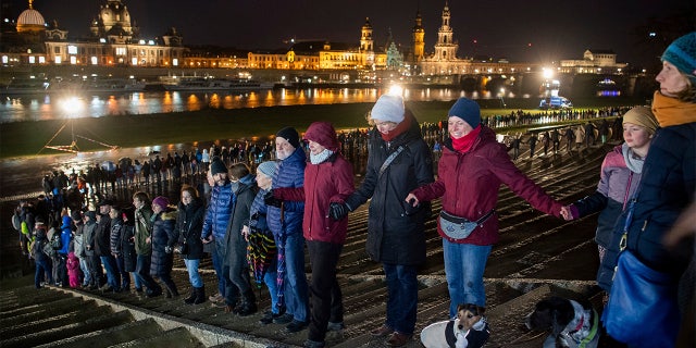 People form a human chain on the banks of the Elbe river with the historical old town in background, marking the 75th anniversary of the destruction of Dresden in the Second World War, in Dresden, Germany. (Robert Michael/dpa via AP)