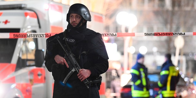 A police officer stands guard near the scene in front of a restaurant after a shooting in central Hanau, Germany Thursday, Feb. 20, 2020. Eight people were killed in shootings in the German city of Hanau on Wednesday evening, authorities said. (Boris Roessler/dpa via AP)