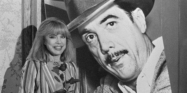 Actress Terry Moore stands before a giant poster of the late billionaire Howard Hughes.