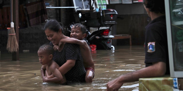 A woman carries her children through flood waters at a flooded neighborhood in Jakarta, Indonesia.