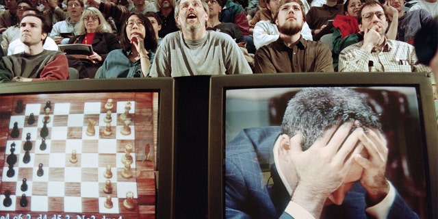 Chess enthusiasts watch World Chess champion Garry Kasparov on a television monitor as he holds his head in his hands at the start of the sixth and final match against IBM's Deep Blue computer in New York. Kasparov lost this match in just 19 moves giving overall victory to Deep Blue with a score of 2.5-3.5. / AFP / STAN HONDA (Photo credit should read STAN HONDA/AFP via Getty Images)