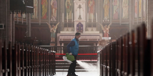 A worker wearing a face mask sprays disinfectant as a precaution against the new coronavirus at Myeongdong Cathedral in Seoul, South Korea, Wednesday, Feb. 26, 2020. (Lee Ji-eun/Yonhap via AP)