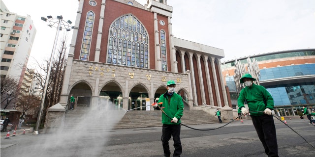 Workers wearing face masks spray disinfectant as a precaution against the new coronavirus in front of Myungsung Church in Seoul, South Korea, Wednesday, Feb. 26, 2020. (Yun Dong-jin/Yonhap via AP)