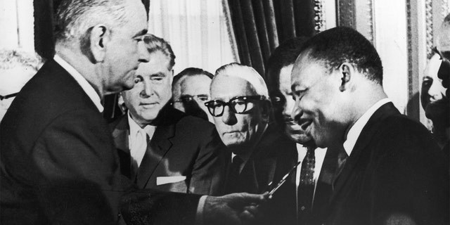 President Lyndon B. Johnson (far left) hands a pen to civil rights leader Rev. Martin Luther King Jr. (at right) during the signing of the Voting Rights Act as officials look on behind them, Washington, D.C., August 6, 1965. 