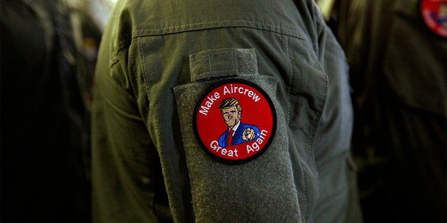 A service member wears a patch that says "Make Aircrew Great Again" as they listen to President Donald Trump speak to troops at a Memorial Day event aboard the USS Wasp in Yokosuka, Japan. The patch includes a likeness of Trump. (AP Photo/Evan Vucci)