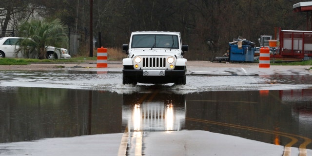 A vehicle carefully passes through a flooded street in downtown Jackson, Miss., as flooding from the Pearl River continues to impact several communities along its bank, Sunday, Feb. 16, 2020.