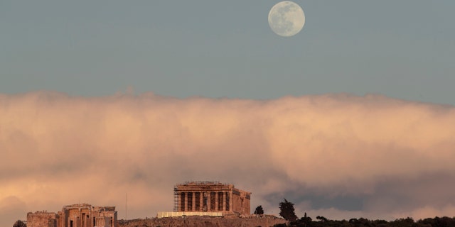 The moon rises behind the ancient Acropolis hill with the 500 BC Parthenon temple in Athens, on Saturday, Feb. 8, 2020.