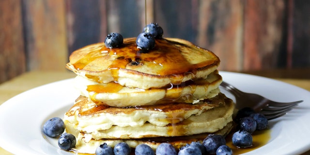 A stack of homemade blueberry pancakes with fresh blueberries and maple syrup is shown here. Busy moms and dads can defrost and then reheat pancakes that are made ahead of time. 