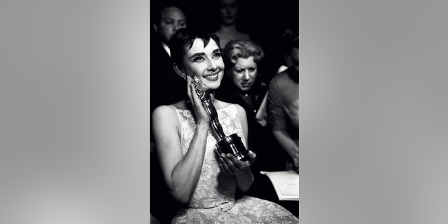 Actress Audrey Hepburn affectionately holding Oscar award she won for her performance in the movie 'Roman Holiday' at the Academy Awards ceremony in New York City.