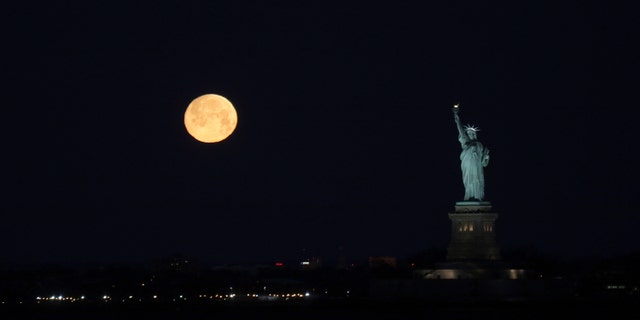 The almost full Snow moon sets beside the Statue of Liberty, photographed from Red Hook, Brooklyn on the morning of Feb. 8, 2020.