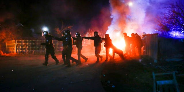 Ukrainian riot police run to push protesters, who planned to stop buses carrying passengers evacuated from the Chinese city of Wuhan, outside Novi Sarzhany, Ukraine, Thursday, Feb. 20, 2020. 