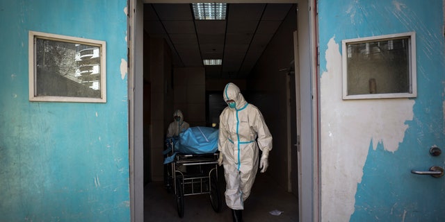 In this Sunday, Feb. 16, 2020, photo, medical workers move a person who died from COVID-19 at a hospital in Wuhan in central China's Hubei province. Chinese authorities on Monday reported a slight upturn in new virus cases and hundred more deaths for a total of thousands since the outbreak began two months ago. (Chinatopix via AP)