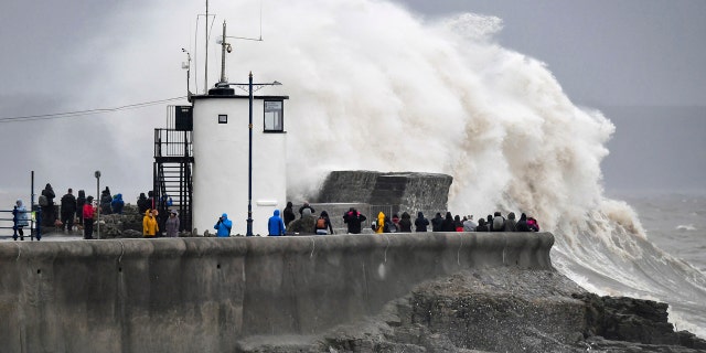 People watch waves and rough seas pound against the harbor wall at Porthcawl in Wales, as Storm Dennis sweeps across the country, Saturday Feb. 15, 2020.