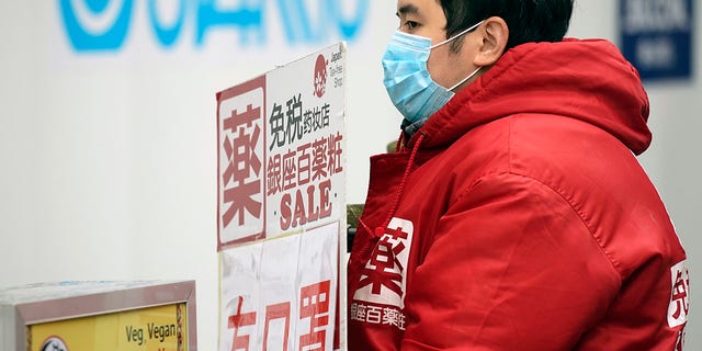 A man holds a shop advertisement saying "We have masks" in Ginza shopping district Wednesday, Feb. 26, 2020, in Tokyo. At a government task force meeting Wednesday on the virus outbreak, Japan's Prime Minister Abe said he was asking organizers to cancel or postpone major sports or cultural events over the next two weeks.
