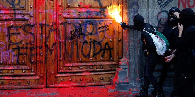 A masked protester sprays fire at the entrance to the National Palace, the presidential office and residence, after demonstrators covered it in fake blood and the Spanish message: 